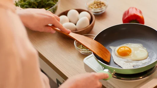 Warm-toned close up of unrecognizable young woman cooking eggs on frying pan while preparing healthy breakfast in morning, copy space