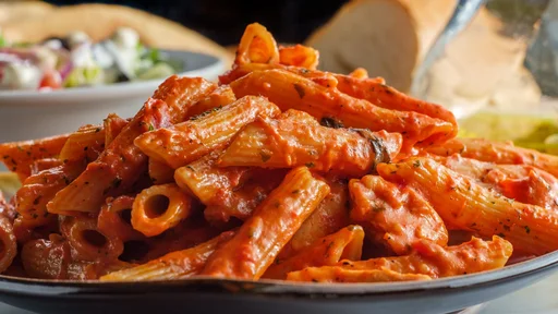 Italian penne pasta in creamy vodka tomato sauce with grilled chicken on marble kitchen table