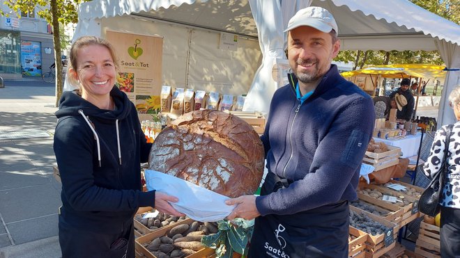 Daniela Pečnik in Marian Tomažej na tržnici v Celovcu, med njima pa 10-kilogramski hlebec kmečkega kruha.