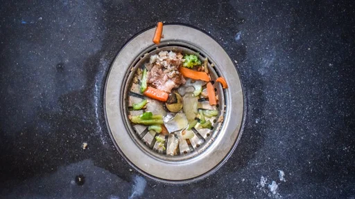 A dirty sink with leftover food bits that clog up the flow of water.
