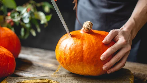 A woman chef cleans an orange pumpkin to prepare for baking. Concept autumn food in a cozy dark wooden kitchen with yellow flowers (A woman chef cleans an orange pumpkin to prepare for baking. Concept autumn food in a cozy dark wooden kitchen with yel