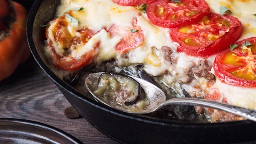Fresh homemade moussaka in iron skillet on rustic wooden background with ingredients. Greek cuisine.