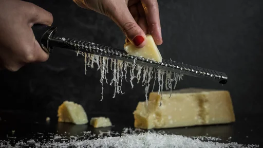 Hand of a woman grating parmesan cheese on a black background. Dark food. Italian cheese Parmigiano Reggiano (Hand of a woman grating parmesan cheese on a black background. Dark food. Italian cheese Parmigiano Reggiano, ASCII, 109 components, 109 byte