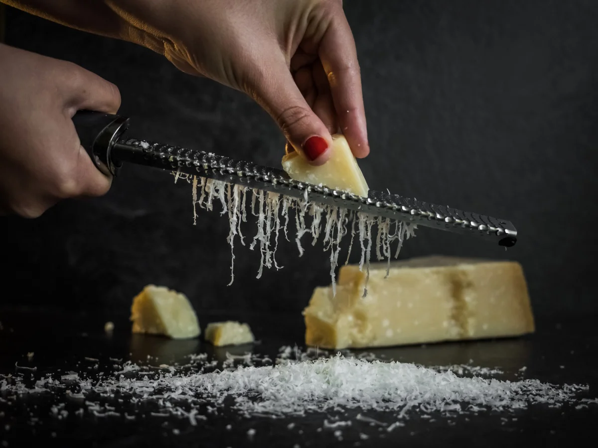 Hand of a woman grating parmesan cheese on a black background. Dark food. Italian cheese Parmigiano Reggiano (Hand of a woman grating parmesan cheese on a black background. Dark food. Italian cheese Parmigiano Reggiano, ASCII, 109 components, 109 byte