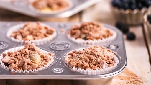 Scooping cinnamon and sugar topping on blueberry muffin batter.