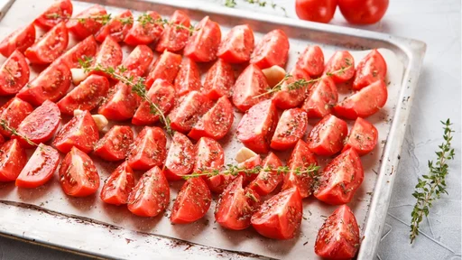 Sliced raw tomatoes with thyme prepared for drying on baking sheet against light background