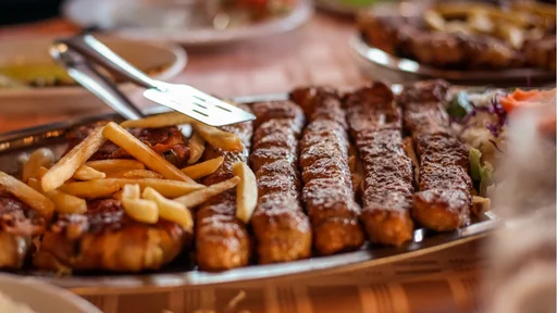 Typical balkan meal in a restaurant, consisting of cevapcici, fries and other meat and vegetables. Food served on a tin plate in a restaurant.