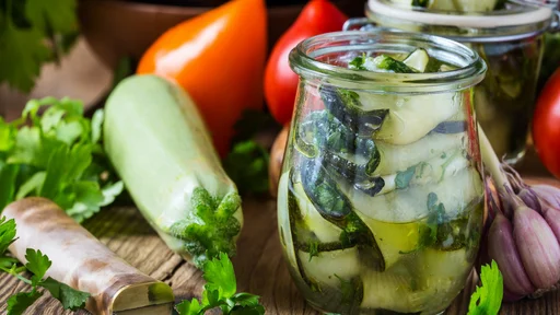 Canned zucchini and fresh vegetables. Sliced zucchini with parsley and garlic, homemade vegetables preserves in glass jar