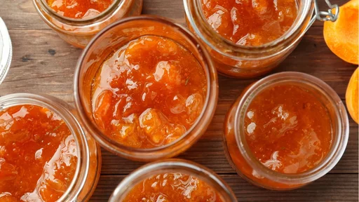 Jars with tasty apricot jam on wooden table