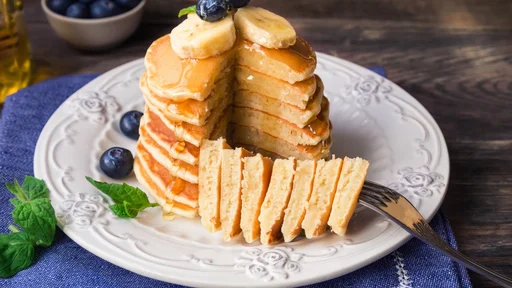 Stack of homemade pancakes with blueberries, banana and honey on rustic wooden background.