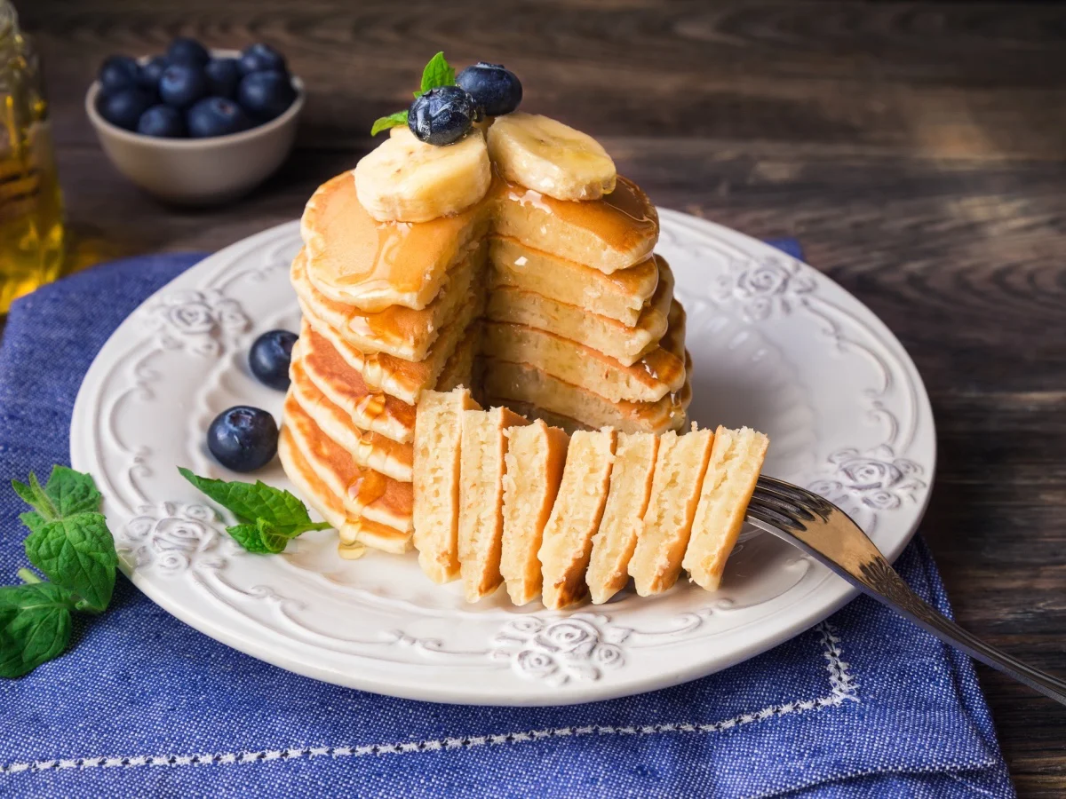 Stack of homemade pancakes with blueberries, banana and honey on rustic wooden background.