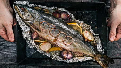 Whole salmon fish baked on tray in foil sheet with lemon, onions and spices. Flat lay
