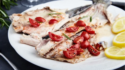 Delicious baked trout with cherry tomatoes, olive oil, lemon juice and fresh rosemary on white plate with lemon slices and fork. Behind blurred glass of red wine, rosemary and towel. Black background (Delicious baked trout with cherry tomatoes, olive