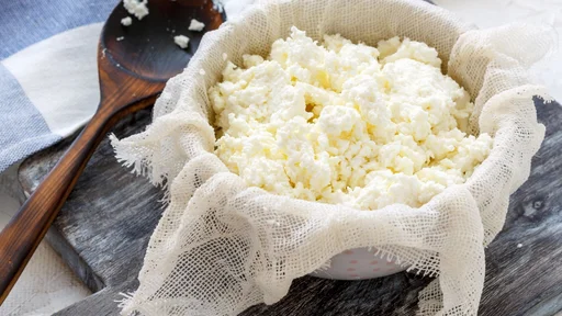 Homemade fresh cottage cheese in gauze and a bowl on the table with linen.