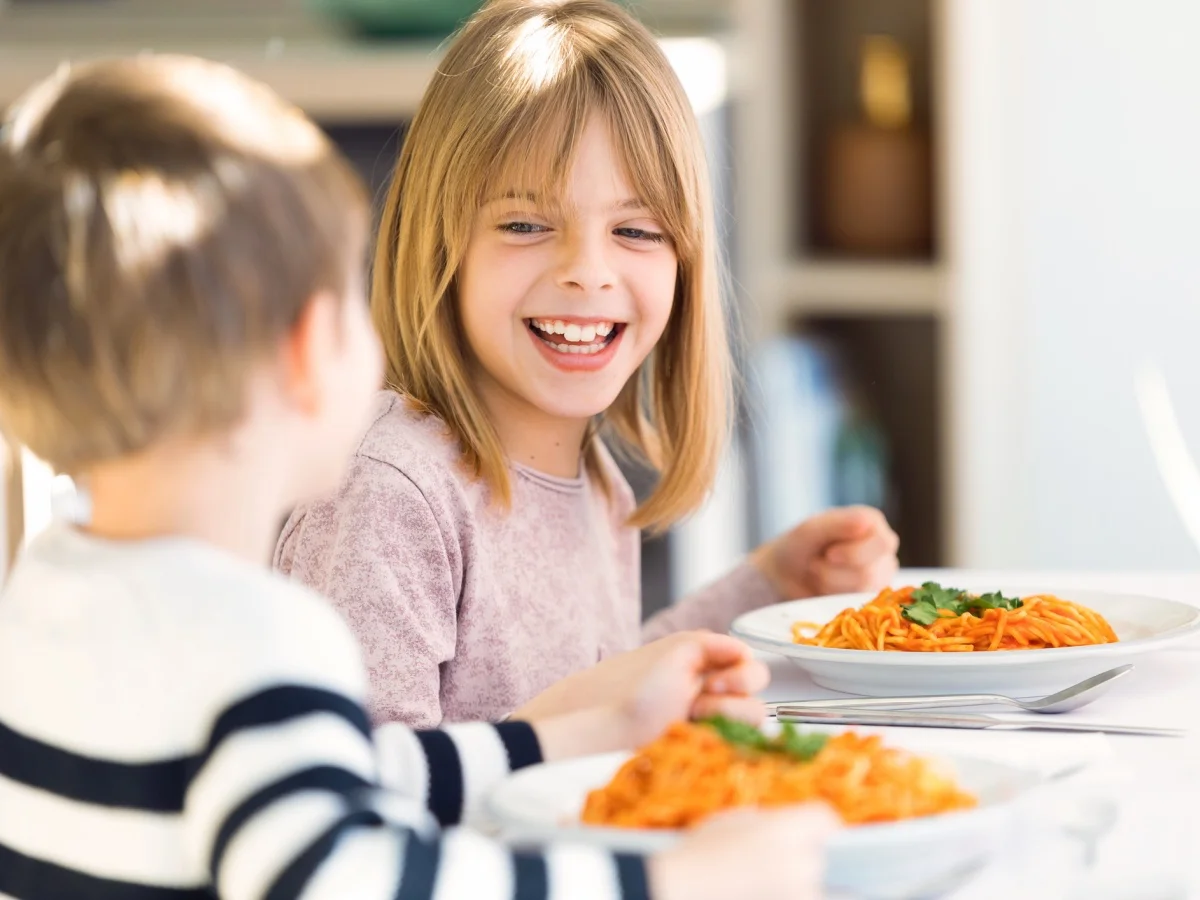 Shot of smiling children having fun while eating spaghetti with tomato sauce in the kitchen at home.
