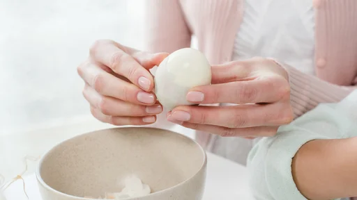 Close-up partial view of young woman peeling boiled egg