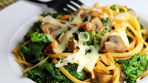 Linguine with mushrooms, kale and muenster cheese in a white bowl