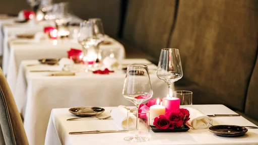 Romantic table settings in a restaurant with centrepieces of burning candles and red roses and elegant glassware for an intimate dinner for two (Romantic table settings in a restaurant with centrepieces of burning candles and red roses and elegant gla