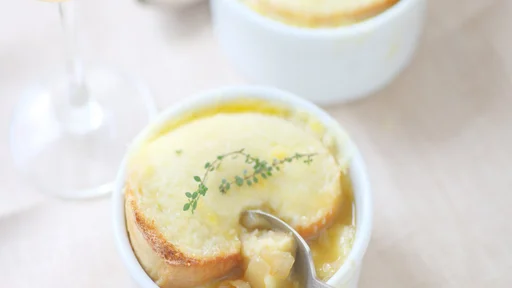 Small white bowls of onion soup with melted cheese toast and fresh thyme