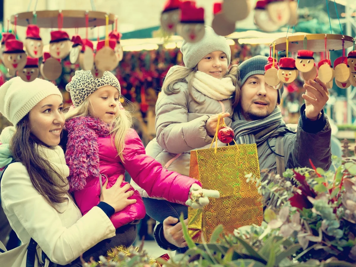 Happy smiling family of four buying Caga Tio at Christmas market. Focus on woman and ittle girl
