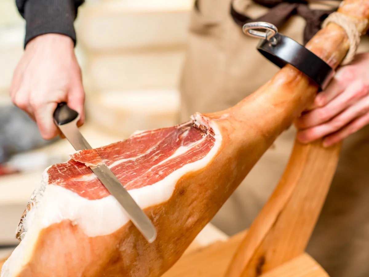 Cutting with long knife prosciutto leg in the food store