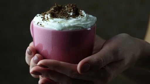 Female hands holding a pink cup with cappuccino and chocolate
