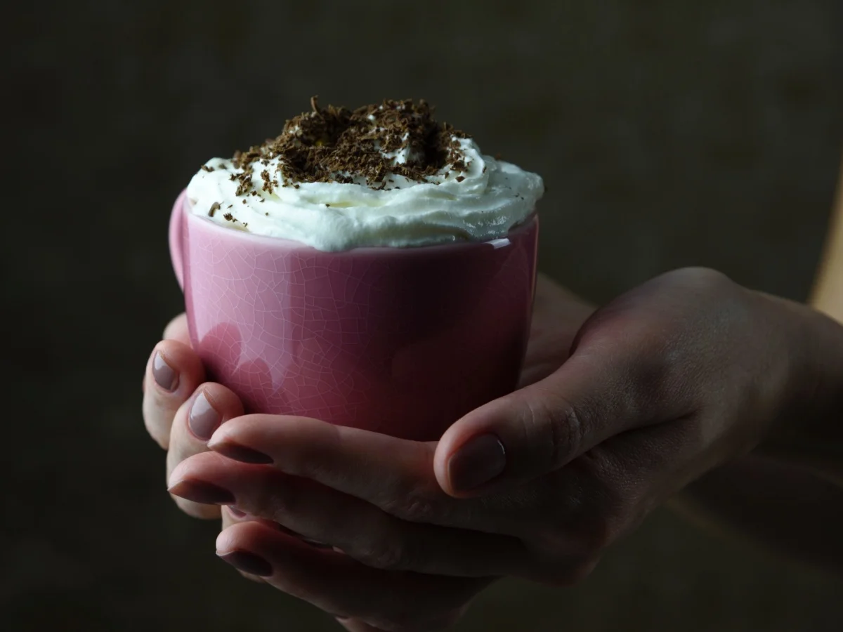 Female hands holding a pink cup with cappuccino and chocolate