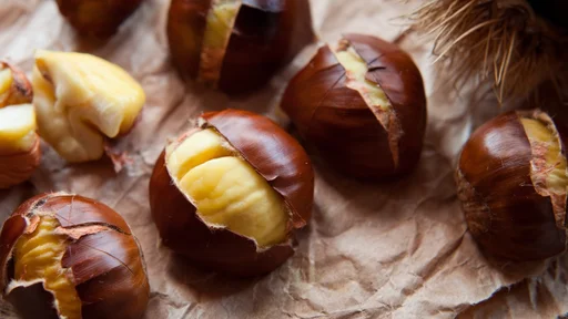Traditional Christmas dish - Ripe Sweet Roasted Chestnuts, cracked shells after put to the fire, natural paper and old wooden rustic background.