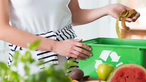 Woman recycling organic kitchen waste by composting in green container during preparation of meal