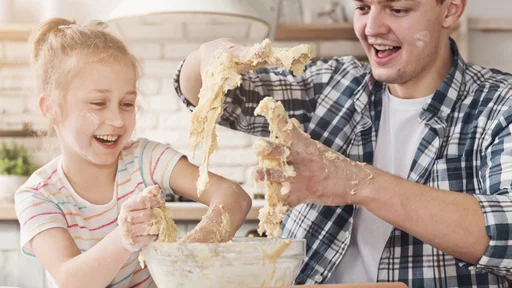 Cute little girl and her father kneading dough and smiling while baking in kitchen at home. Fathers day, family, holiday concept