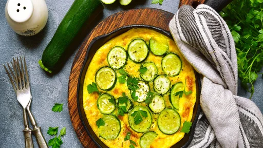 Oven baked omelette with zucchini in a cast iron pan over dark grey slate,stone or concrete background.Top view with copy space.