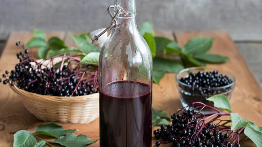 A bottle of elderberry syrup on a wooden table, with fresh elderberries in the background
