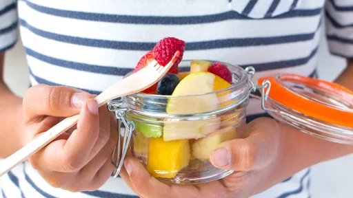Little girl hands eating a fruit salad on a jar. Healthy snack for children concept