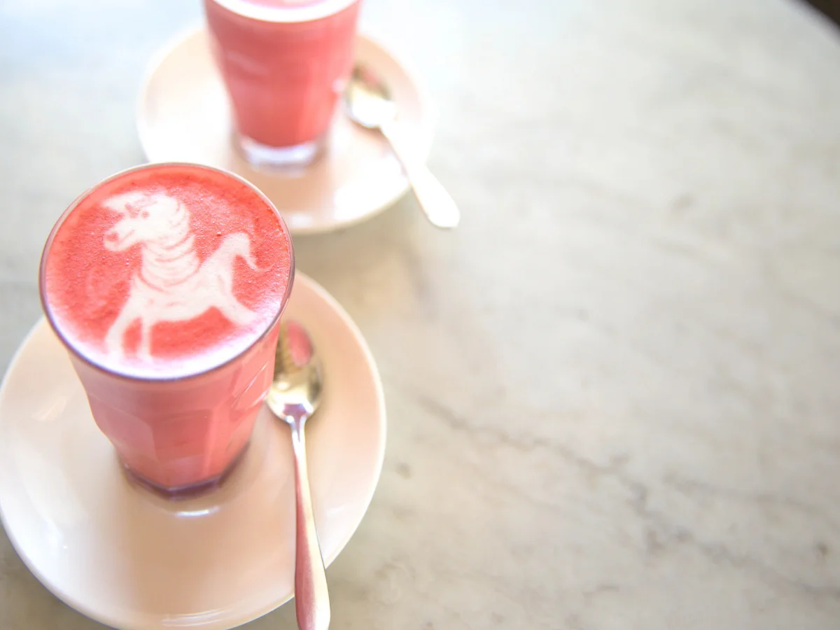 Beetroot latte on marble background with unicorn art on the top. Flat lay view. Color trendy latte.