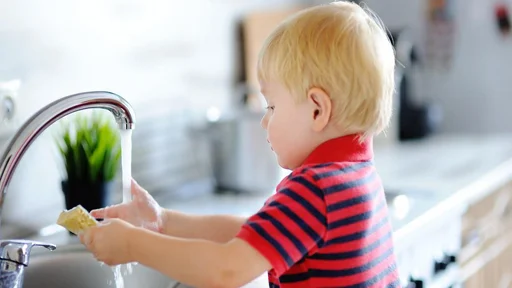 Cute toddler boy washing dishes in domestic kitchen. Child having fun with helping his parents with housework