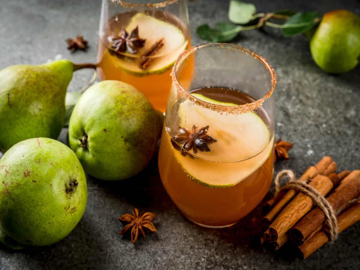 Autumn drinks. Mulled wine. Traditional autumn spicy cocktail with pear, cider and chocolate syrup, with cinnamon, anise, brown sugar. On black stone table. Copy space