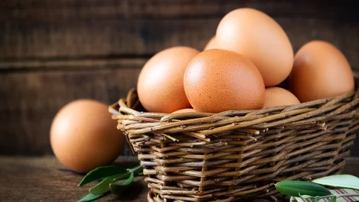 Fresh eggs in a rustic willow basket against dark wooden background