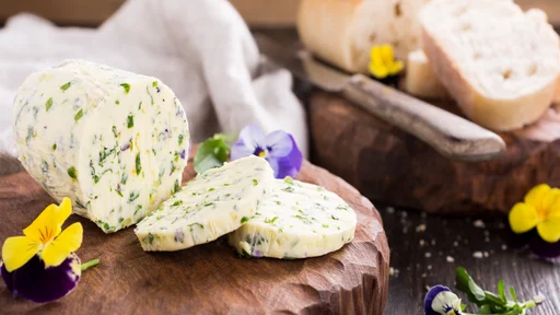 Herb butter with edible flowers on wooden cutting board, healthy food.