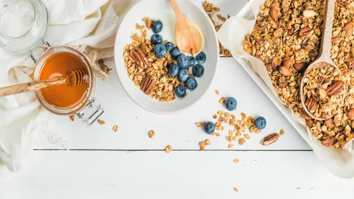 Healthy breakfast set. Oat granola with nuts, yogurt, honey and blueberries in bowl on white wooden background, top view, copy space, horizontal composition