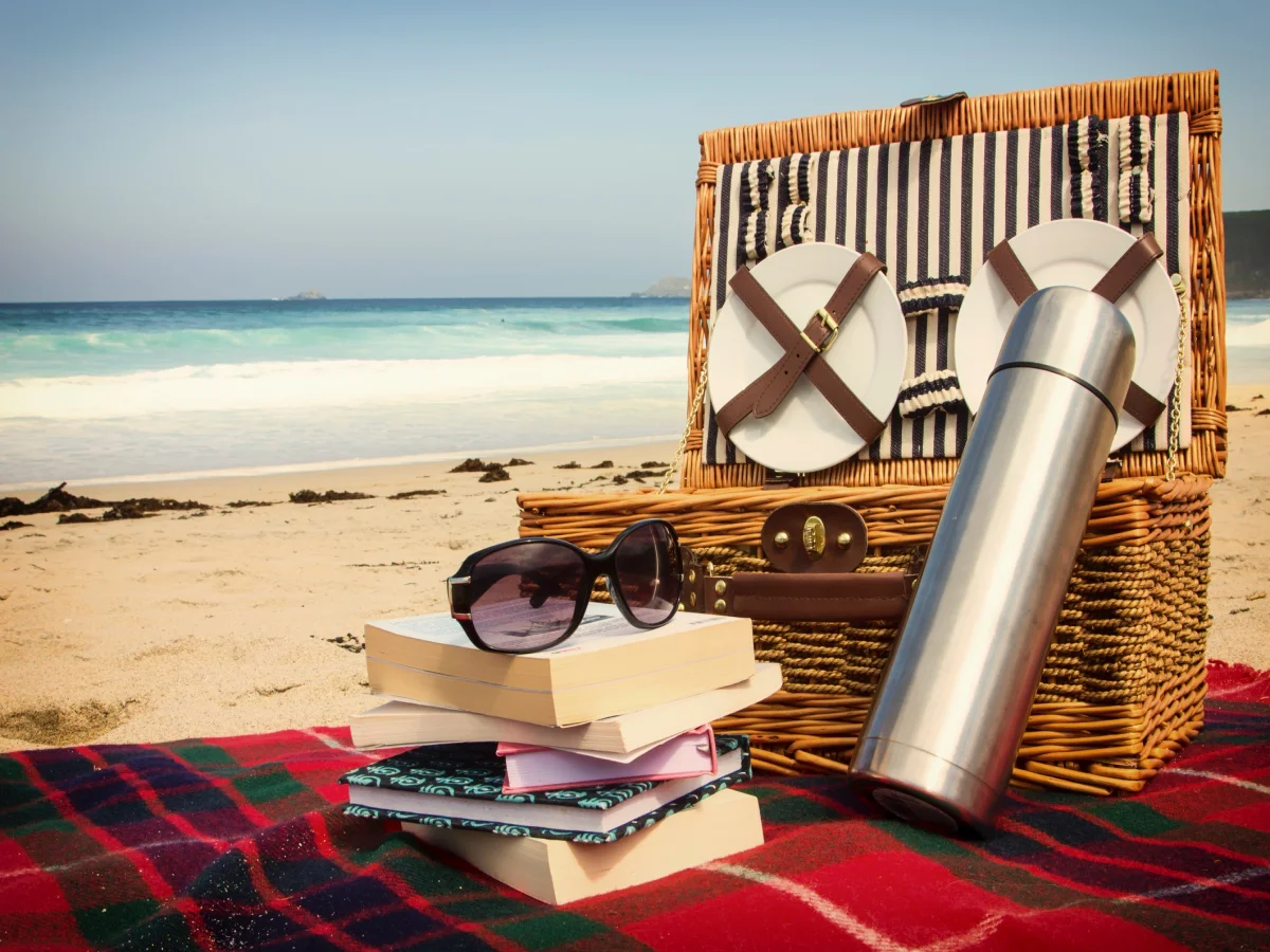 Landscape colour photograph of a beach picnic, books and sunglasses