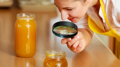 Mature woman female inspecting testing honey food with magnifying glass.