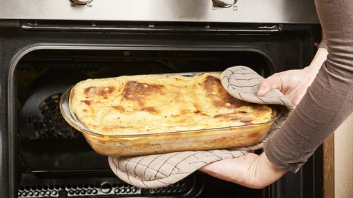 A woman cook takes out a freshly baked lasagna with melted cheese and gratin from the hot oven in her kitchen