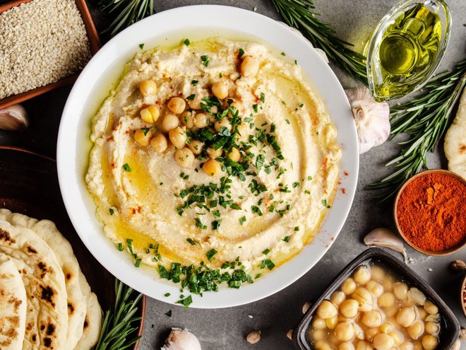 Hummus topped with chickpeas, olive oil and green coriander leaves on stone table with pita bread and spices aside. Flat lay (Hummus topped with chickpeas, olive oil and green coriander leaves on stone table with pita bread and spices aside. Flat lay,