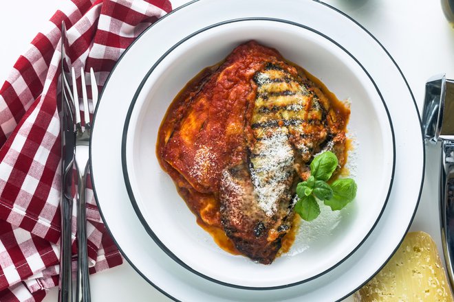 Italian melanzane alla parmigiana dish, made of eggplants and tomatoes on a table, served in a plate. with cheese and basil. traditional cuisine (Italian melanzane alla parmigiana dish, made of eggplants and tomatoes on a table, served in a plate. wit