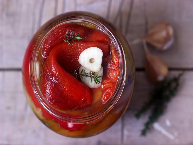 Baked pickled sweet pepper with garlic and thyme in a glass jar. Selective focus.
