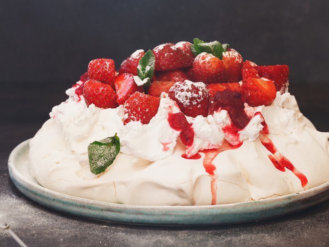 Delicious pavlova cake topped with sweetened whipped cream, balsamic strawberries and cranberry sauce, selective focus
