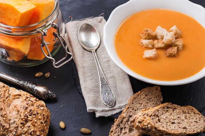 Still life, food and drink, seasonal concept. Autumn spicy pumpkin soup in a white bowl with grain cereal rye bread on a table. Selective focus