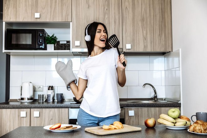 Cooking and fun. At home. Asian girl listen music in headphones and singing in the kitchen