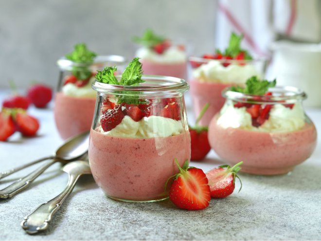 Delicious strawberry mousse with fresh berries and whiped cream in a glass jars on a light background.