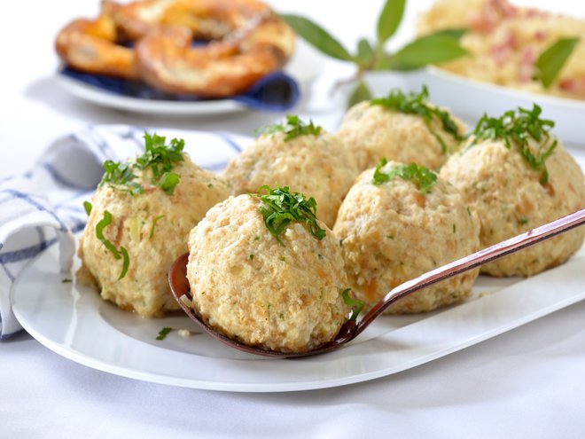 Bavarian bread dumplings served on a white platter, garnished with parsley, sauerkraut with bacon and a pretzel in the background